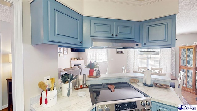 kitchen with electric stove, blue cabinets, a textured ceiling, and exhaust hood