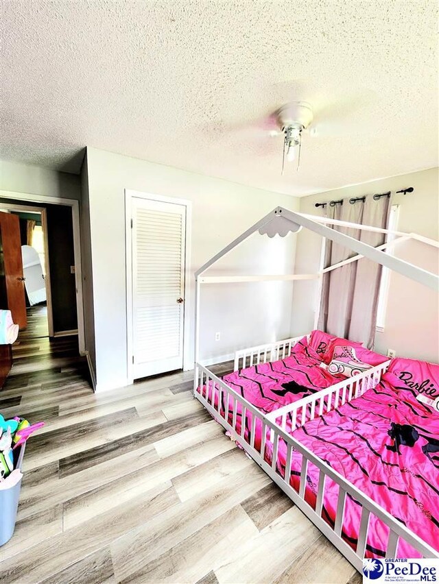 bedroom with ceiling fan, wood-type flooring, a closet, and a textured ceiling