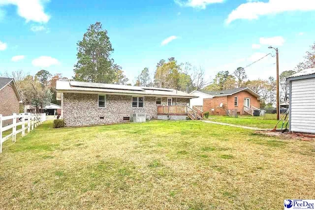 rear view of property featuring a wooden deck, a yard, central AC unit, and solar panels