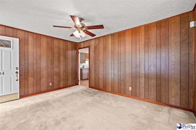 carpeted spare room featuring crown molding, a textured ceiling, ceiling fan, and wood walls