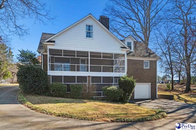 view of side of property with an attached garage, a sunroom, driveway, a lawn, and a chimney