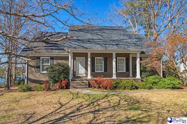 view of front facade featuring a shingled roof, a porch, a front lawn, and brick siding