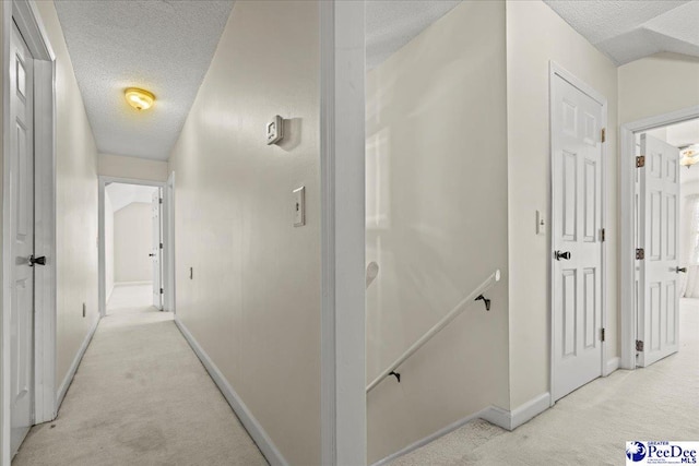 corridor with a textured ceiling, baseboards, an upstairs landing, and light colored carpet