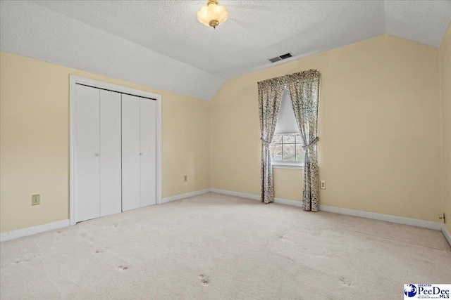 unfurnished bedroom with lofted ceiling, carpet, visible vents, and a textured ceiling