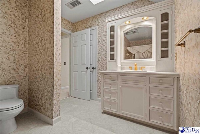 bathroom with toilet, vanity, baseboards, visible vents, and wallpapered walls