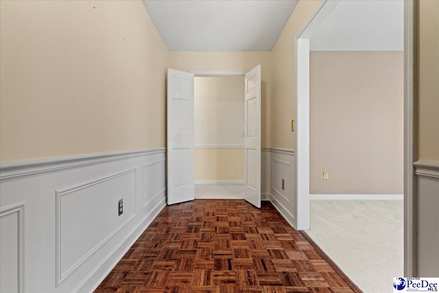 hallway with a textured ceiling, wainscoting, and a decorative wall