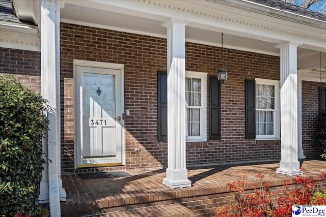 doorway to property with covered porch and brick siding