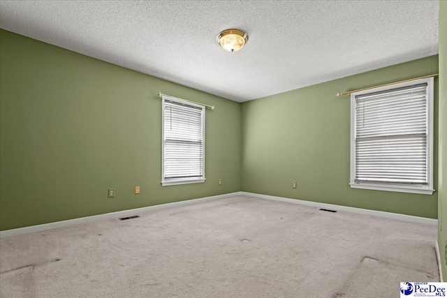 spare room featuring carpet floors, visible vents, a textured ceiling, and baseboards