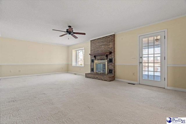 unfurnished living room featuring a wainscoted wall, a brick fireplace, carpet flooring, and a textured ceiling