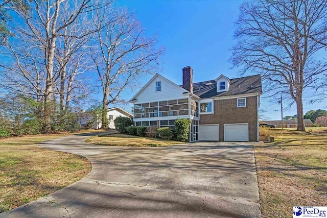 view of front of house with an attached garage, a sunroom, concrete driveway, a front lawn, and a chimney