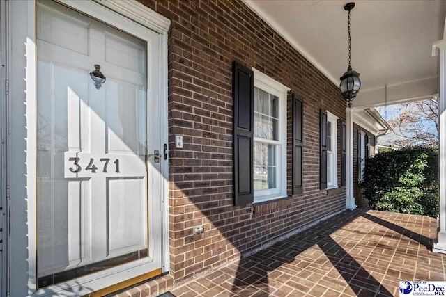 entrance to property featuring a porch and brick siding