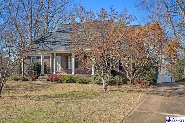 view of front of house featuring covered porch, brick siding, and a front yard