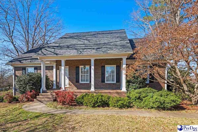 view of front of property featuring brick siding, roof with shingles, and a front yard