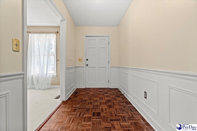 doorway with a textured ceiling and wainscoting