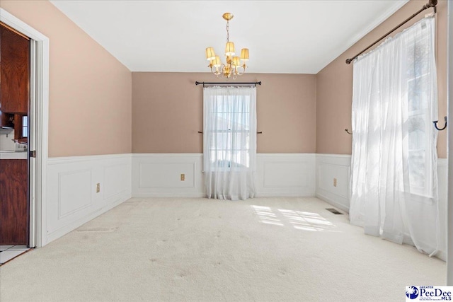 spare room featuring carpet floors, a wainscoted wall, a notable chandelier, and visible vents