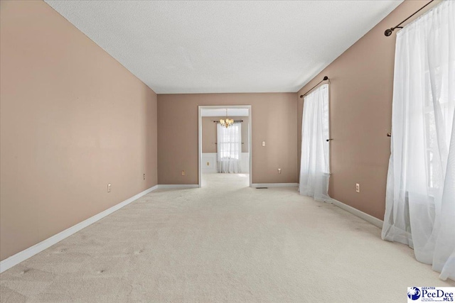 spare room with light carpet, baseboards, a chandelier, and a textured ceiling