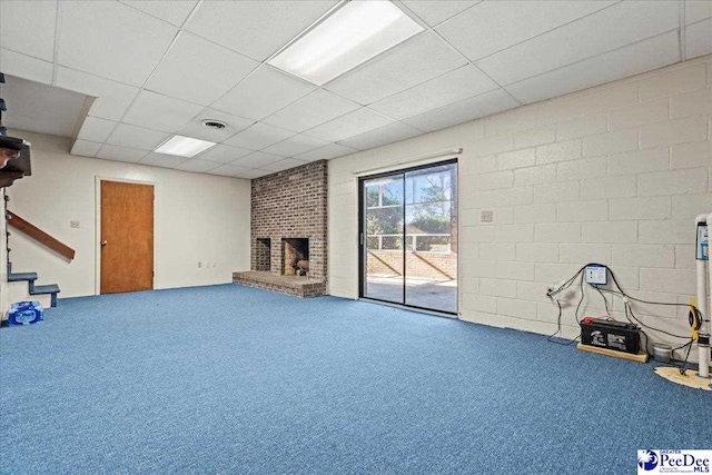 below grade area featuring carpet floors, a brick fireplace, a drop ceiling, and stairway