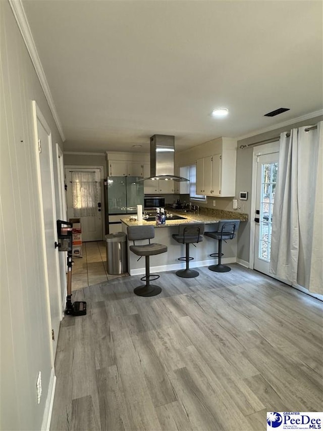 kitchen with island range hood, a kitchen breakfast bar, kitchen peninsula, and light wood-type flooring