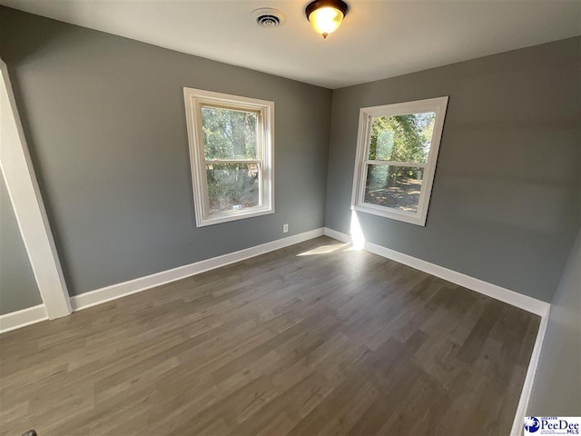 spare room featuring visible vents, baseboards, dark wood-type flooring, and a healthy amount of sunlight