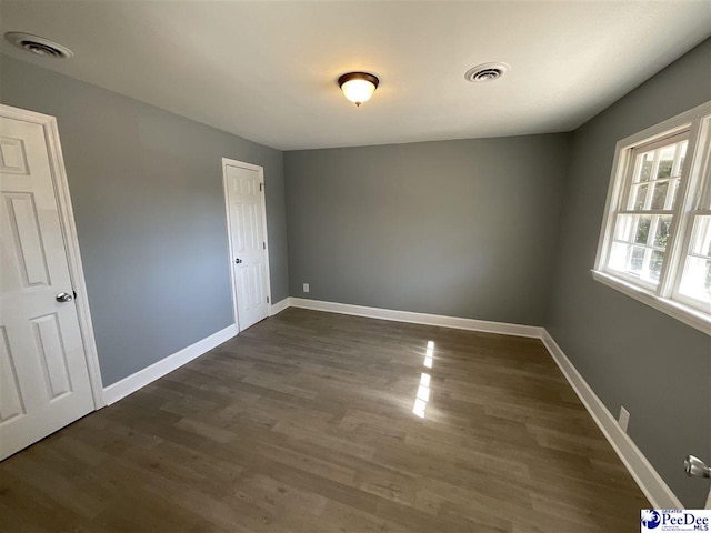 empty room with baseboards, visible vents, and dark wood-style flooring