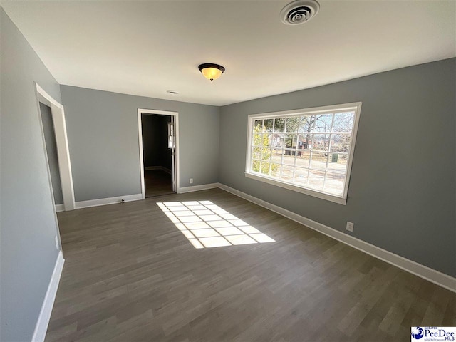 spare room featuring dark wood-style floors, visible vents, and baseboards