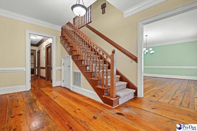 stairs featuring ornamental molding, hardwood / wood-style flooring, a chandelier, and baseboards
