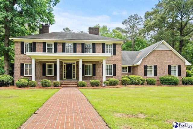 view of front facade with brick siding, a chimney, and a front yard