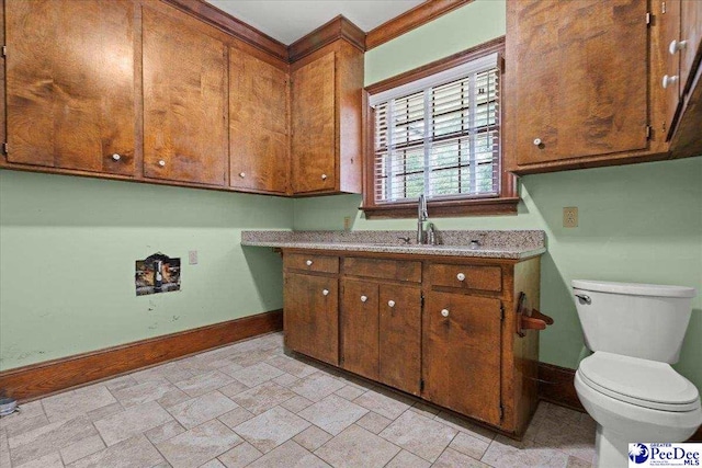 kitchen featuring baseboards, a sink, light countertops, brown cabinets, and light stone finish floors