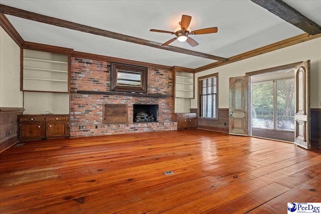 unfurnished living room with built in features, beam ceiling, wood-type flooring, a fireplace, and wainscoting