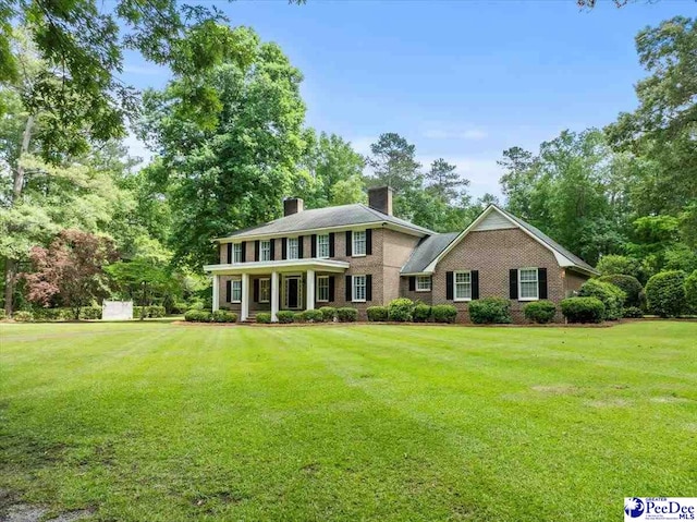 colonial-style house with a chimney, a front lawn, and brick siding
