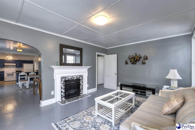 living room featuring dark wood-style floors, arched walkways, baseboards, a tile fireplace, and ornamental molding