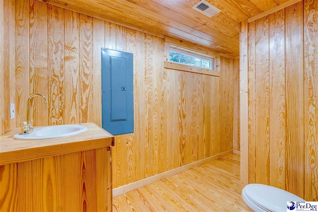 bathroom featuring wood walls, hardwood / wood-style flooring, electric panel, toilet, and wooden ceiling