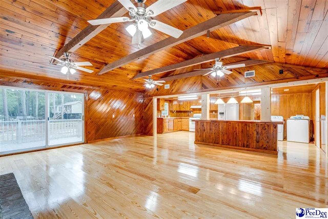 unfurnished living room with washer / dryer, wood ceiling, lofted ceiling with beams, light wood-type flooring, and wooden walls