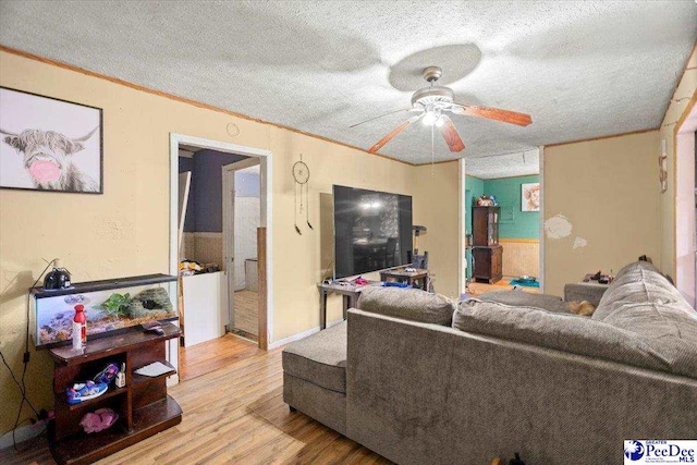 living room with ceiling fan, crown molding, light hardwood / wood-style flooring, and a textured ceiling