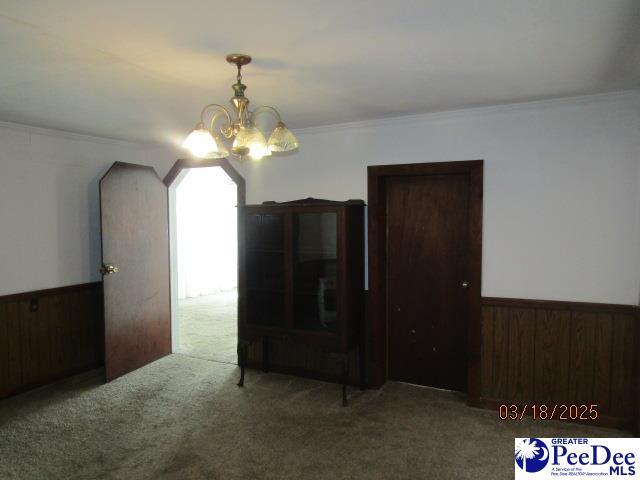 carpeted spare room with a wainscoted wall, a notable chandelier, wooden walls, and crown molding