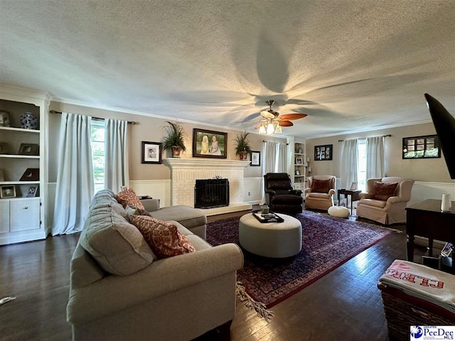 living area featuring ornamental molding, plenty of natural light, dark wood-style flooring, a ceiling fan, and a textured ceiling