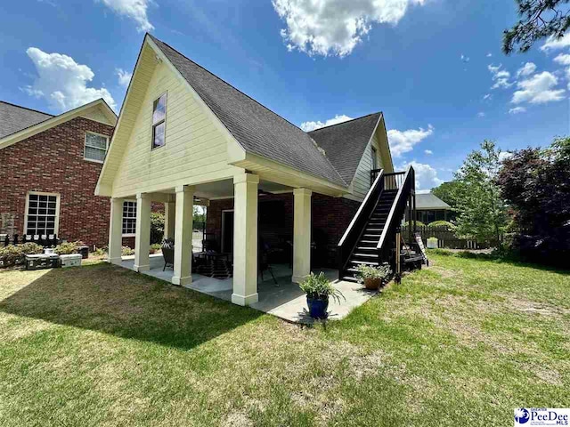 rear view of property with a shingled roof, brick siding, a lawn, and stairway