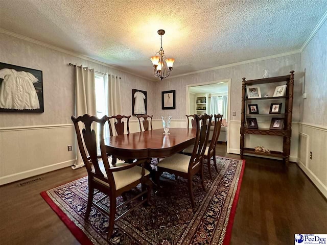 dining space featuring wood finished floors, a textured ceiling, a chandelier, ornamental molding, and wainscoting