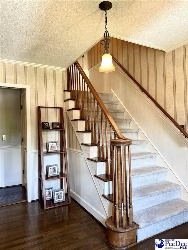 stairway featuring a textured ceiling, wood finished floors, wallpapered walls, ornamental molding, and wainscoting