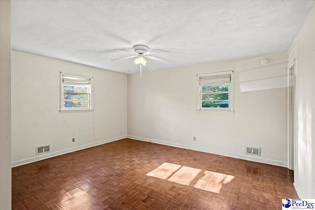 empty room featuring dark parquet flooring, plenty of natural light, ceiling fan, and a textured ceiling