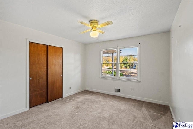 unfurnished bedroom with light carpet, ceiling fan, a closet, and a textured ceiling