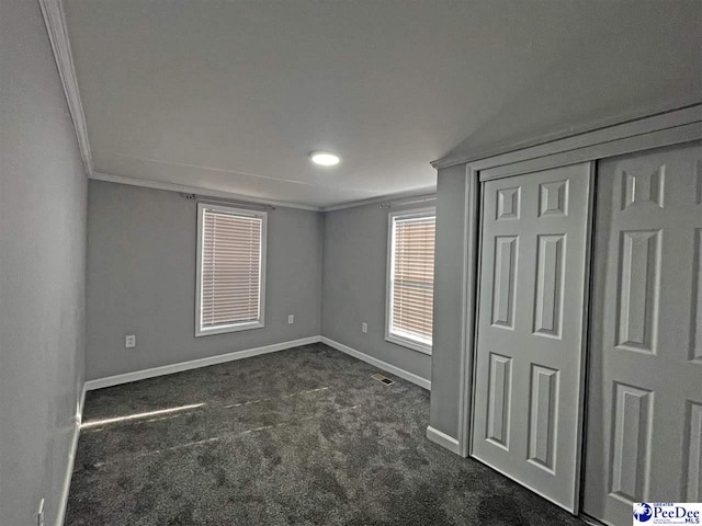 unfurnished bedroom with ornamental molding, dark carpet, and a closet