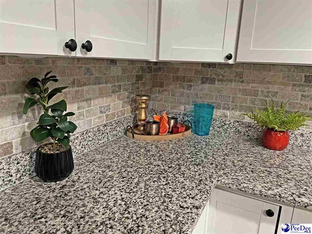 room details featuring light stone countertops, white cabinets, and decorative backsplash