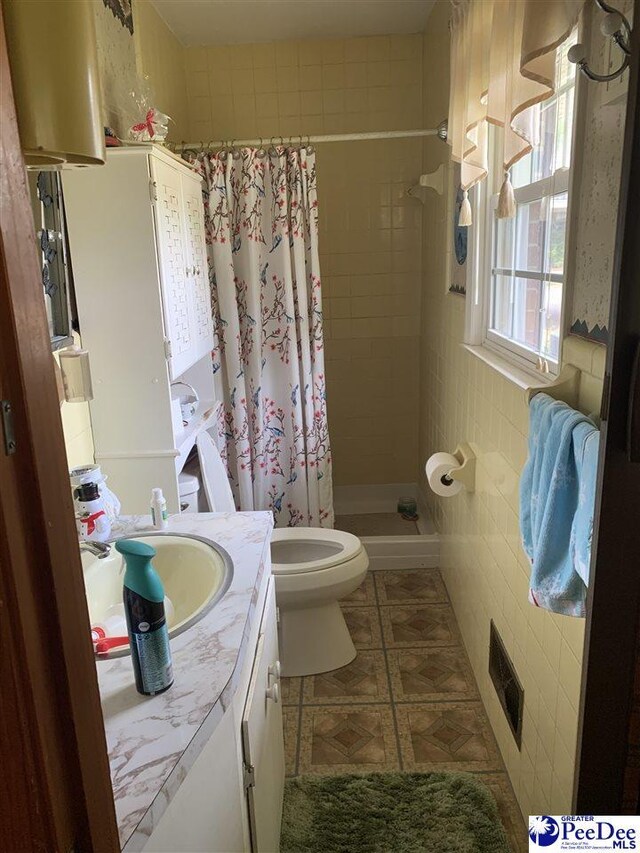 bathroom with toilet, tile walls, vanity, a shower with shower curtain, and tile patterned flooring