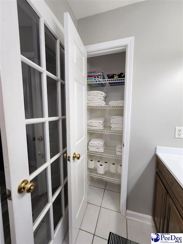 bathroom featuring baseboards, vanity, tile patterned flooring, and a walk in closet