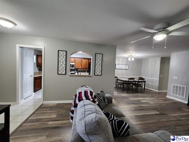living room featuring wood finished floors, visible vents, baseboards, and ceiling fan