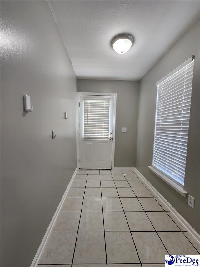 doorway to outside featuring a healthy amount of sunlight, baseboards, and light tile patterned floors
