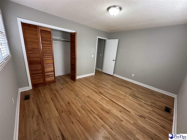 unfurnished bedroom with light hardwood / wood-style flooring, a textured ceiling, and a closet