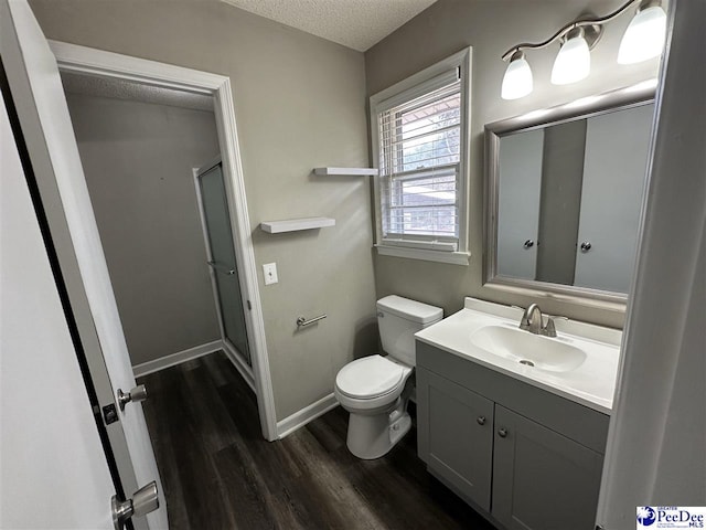 bathroom with vanity, a textured ceiling, toilet, hardwood / wood-style flooring, and a shower with door