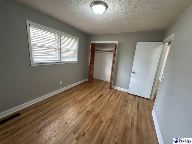 unfurnished bedroom featuring light wood-type flooring, a closet, and a textured ceiling